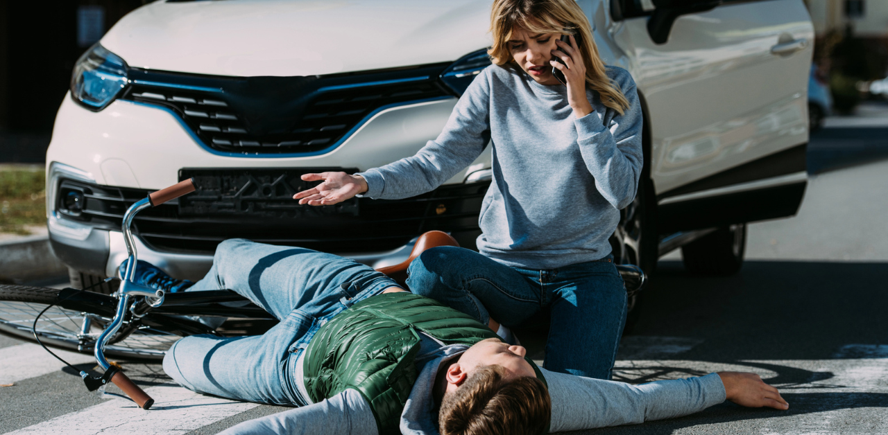 A man riding a bike gets hit by a car and a woman talks on the phone