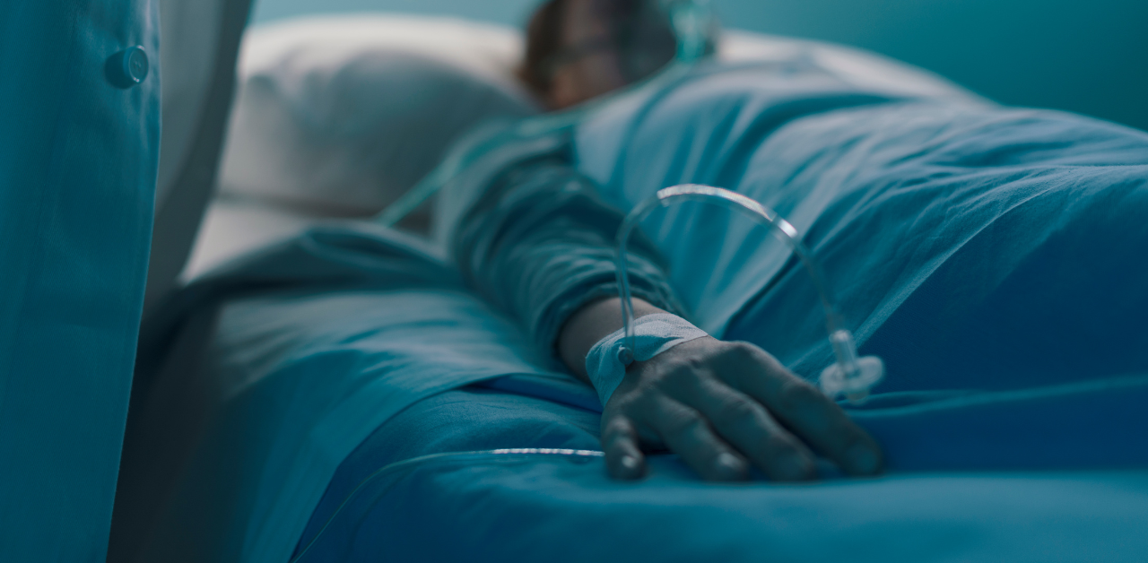 Patient lying in a hospital bed with an IV line attached to their hand in a dimly lit room