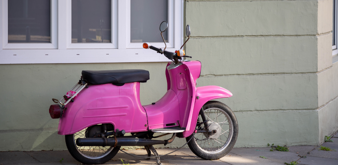 Pink vintage scooter parked beside a pale green wall under a window, adding a colorful urban street detail