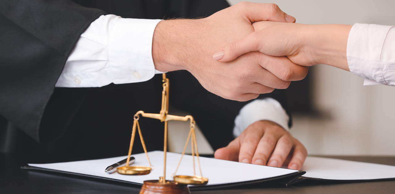 Lawyer and client shaking hands over legal documents, with justice scales symbolizing agreement and legal support