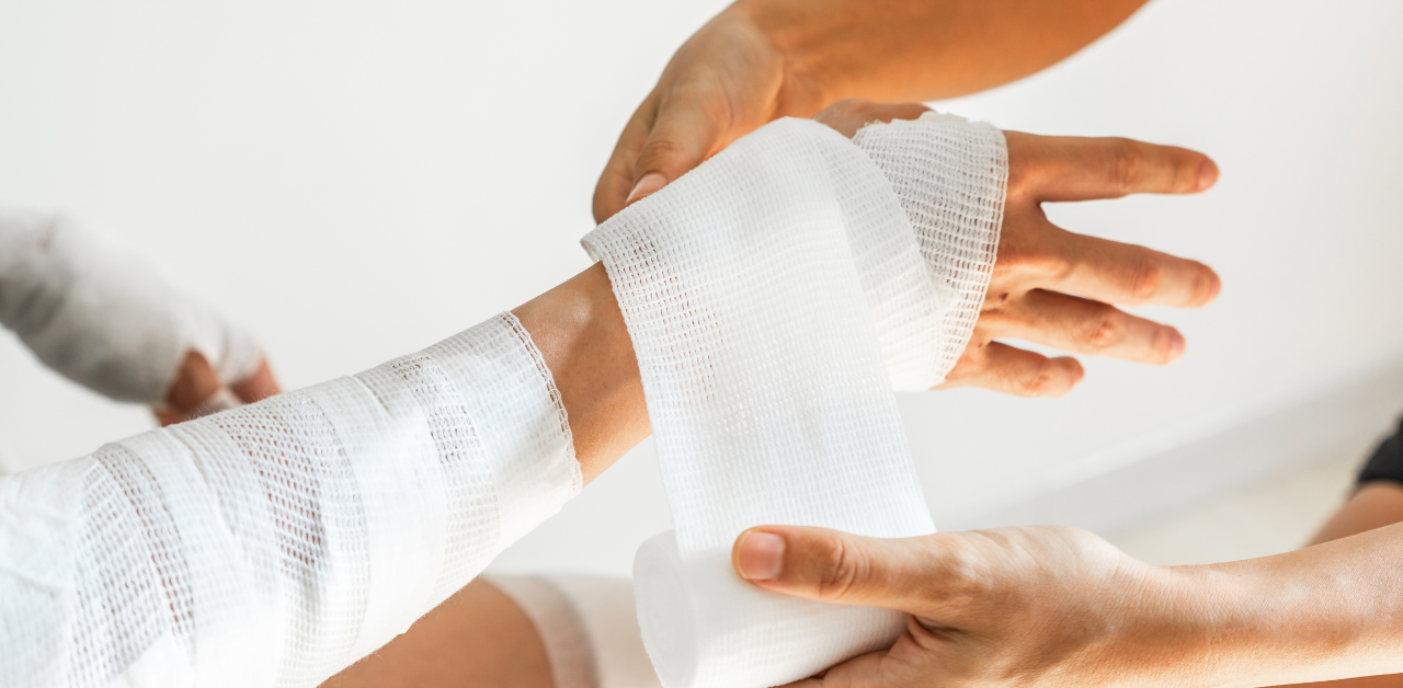 Close-up of a person's injured arm being wrapped in white medical bandages by a caregiver