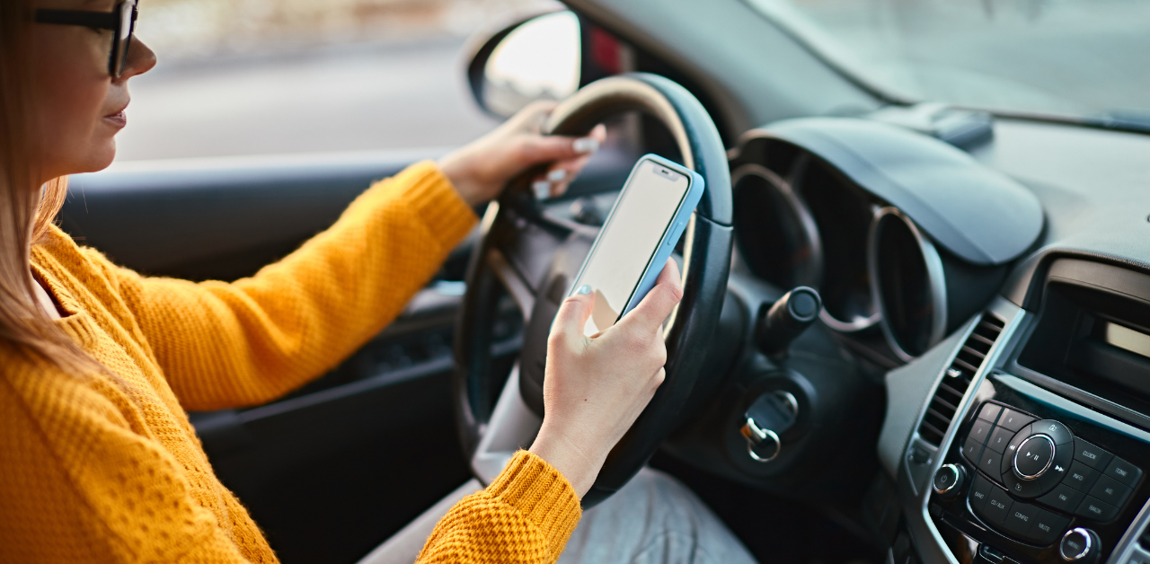 Driver using a phone behind the wheel, showing distracted driving risks to pedestrian safety