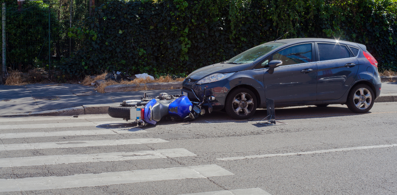 Motorcycle lies on road after crash with a car near a crosswalk, showing a serious motorcycle accident