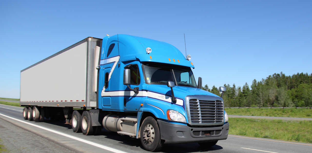 Bright blue semi-truck driving on highway under clear sky