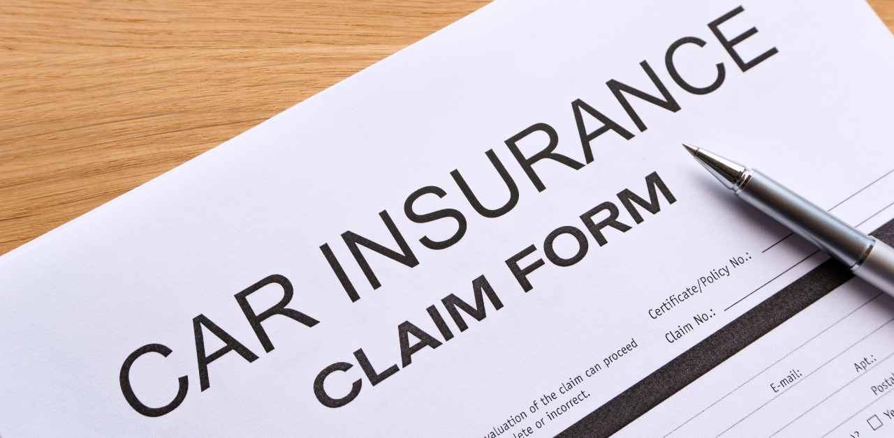 Close-up of a car insurance claim form with a silver pen on a wooden desk