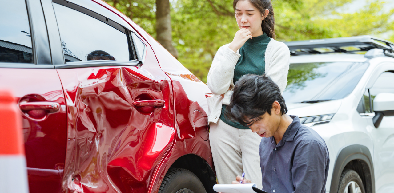 Couple assessing red car damage after collision for insurance claim