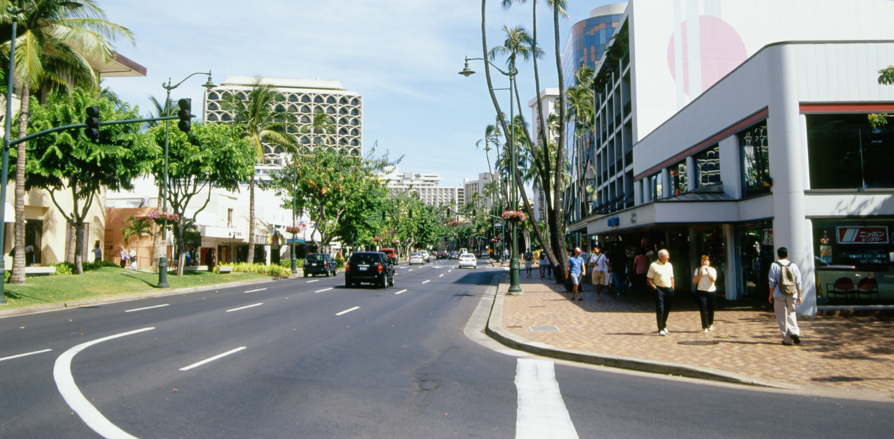 Busy city street with palm trees, shops, and pedestrians in a sunny urban coastal area