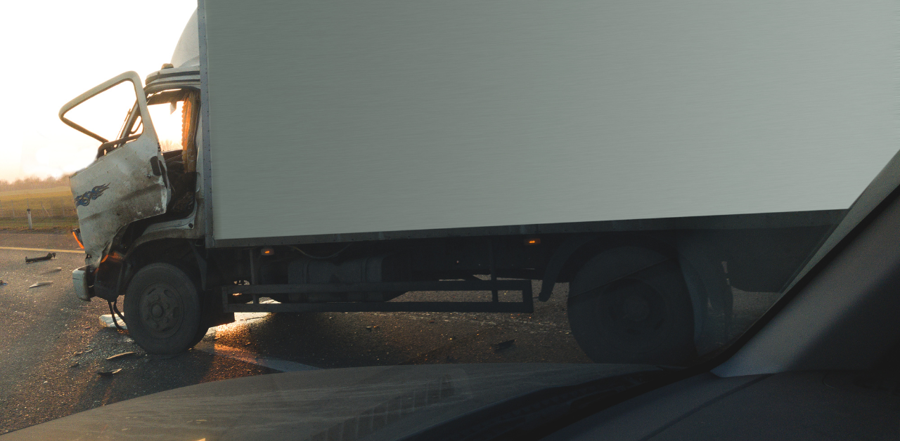Damaged box truck blocking road after collision, with crushed cab and debris scattered across pavement