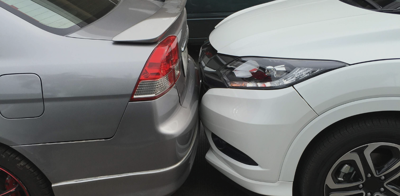 Close-up of two cars involved in a rear-end collision, showing bumper impact damage in a parking area