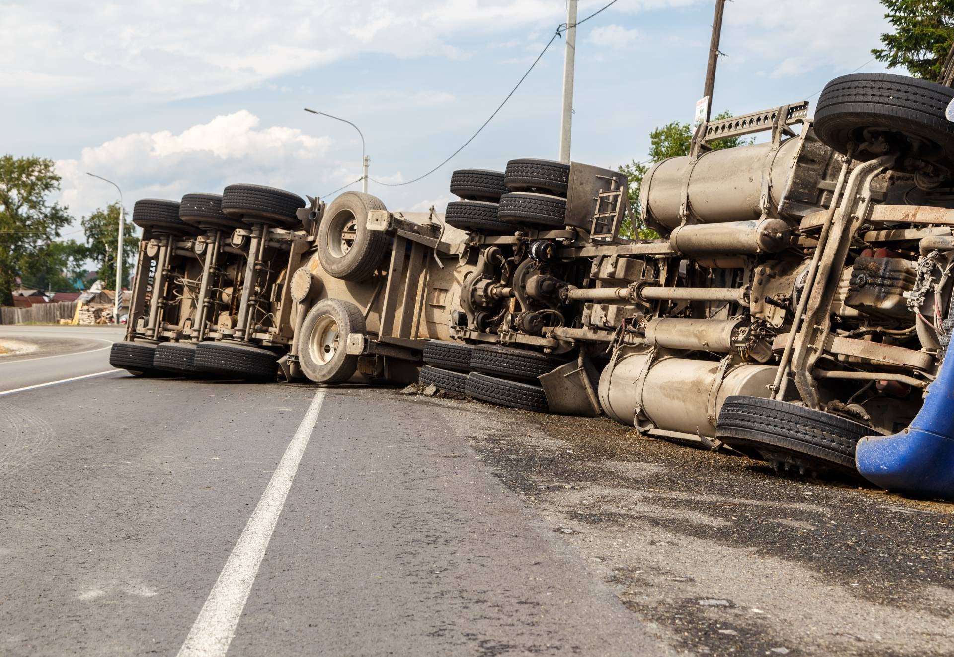 An overturned tanker truck and trailer lying on their sides on a paved road, blocking traffic.