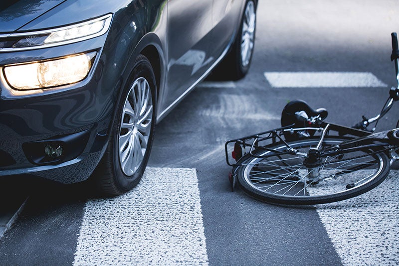 Dark gray car stopped on a crosswalk near a bicycle lying on its side.