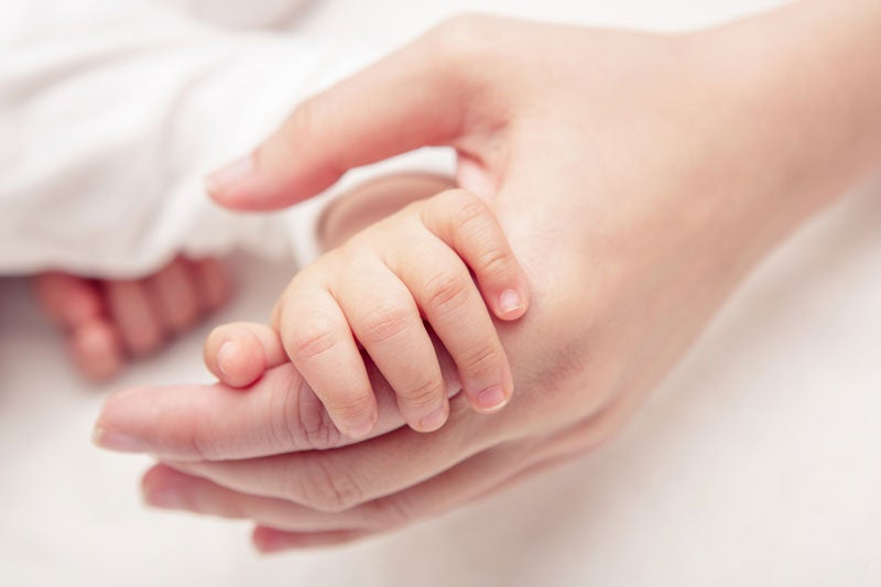 A baby's tiny hand holding an adult's finger, symbolizing protection and new life.