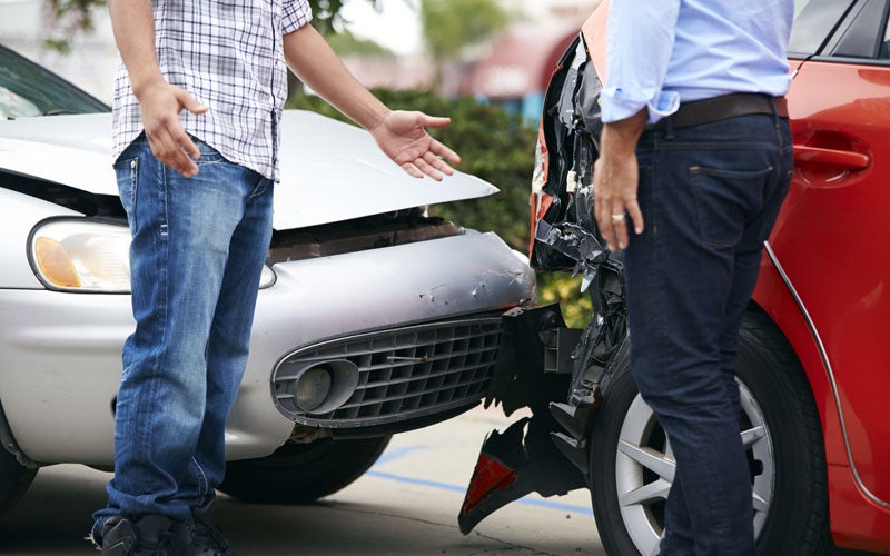 Two men stand between a silver and a red car after a crash, both vehicles showing front-end damage.
