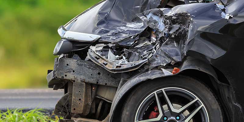 Close-up of the front of a black car, severely damaged and crumpled after a collision.