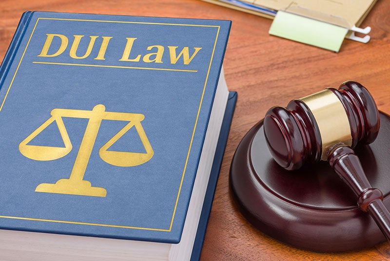 A blue 'DUI Law' book with golden scales of justice and a wooden gavel resting on a wooden desk.
