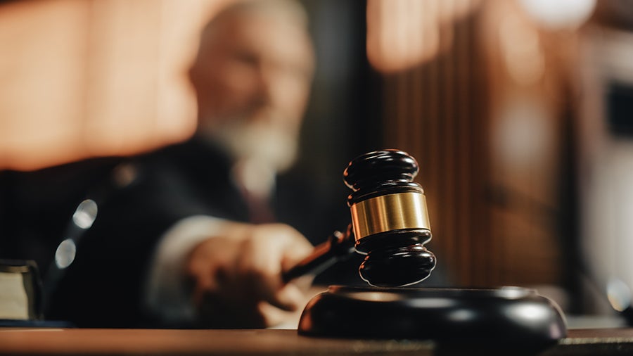A blurred judge in robes holds a gavel above a sounding block in court.