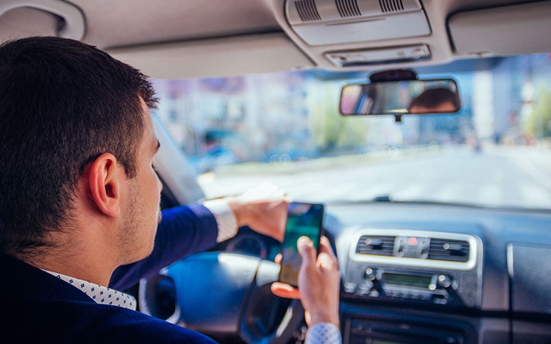 Man driving a car and looking down at his smartphone, clearly distracted from the road.