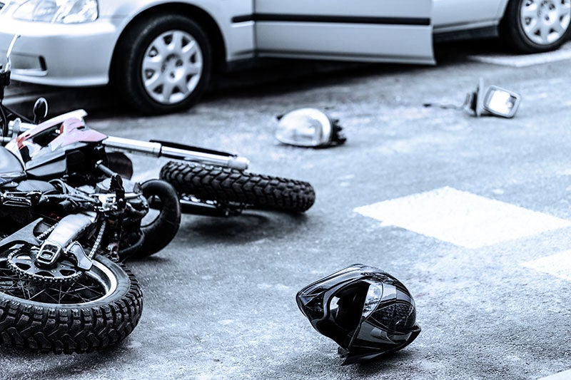 Motorcycle and car with open door after a crash, with a helmet and debris on the asphalt.