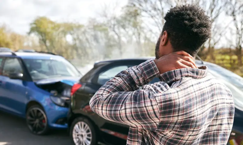 Man rubbing his neck in pain after a car accident damaging a blue and black car.