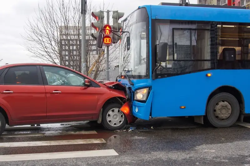 A vivid red car crashed into the side of a prominent blue bus on a city street during the daytime.