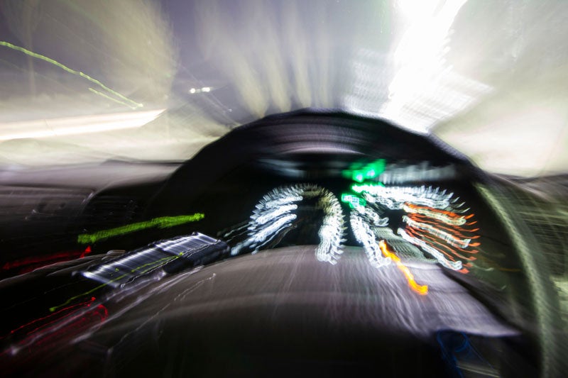 A blurry, surreal car dashboard and view of the road from the driver's perspective, with streaking lights.