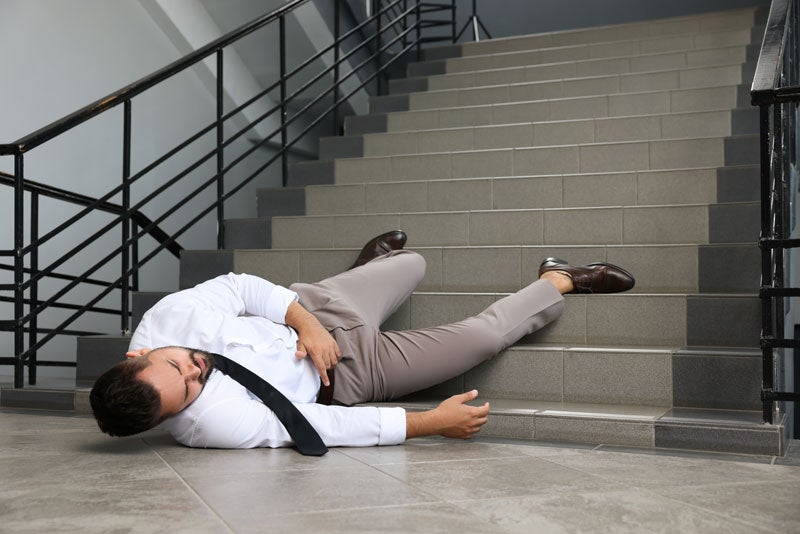A man in a shirt and tie lies unconscious at the bottom of a flight of stairs.