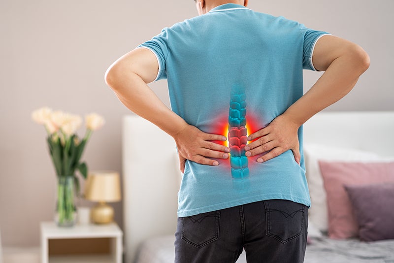 Person holding their lower back with a glowing red and blue spine overlay, indicating back pain.
