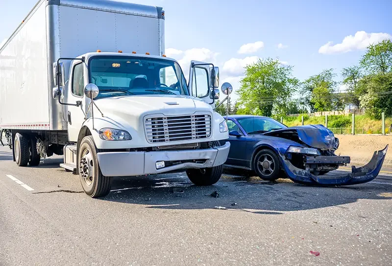 A large white truck involved in an accident with a severely damaged blue car, its front bumper detached.