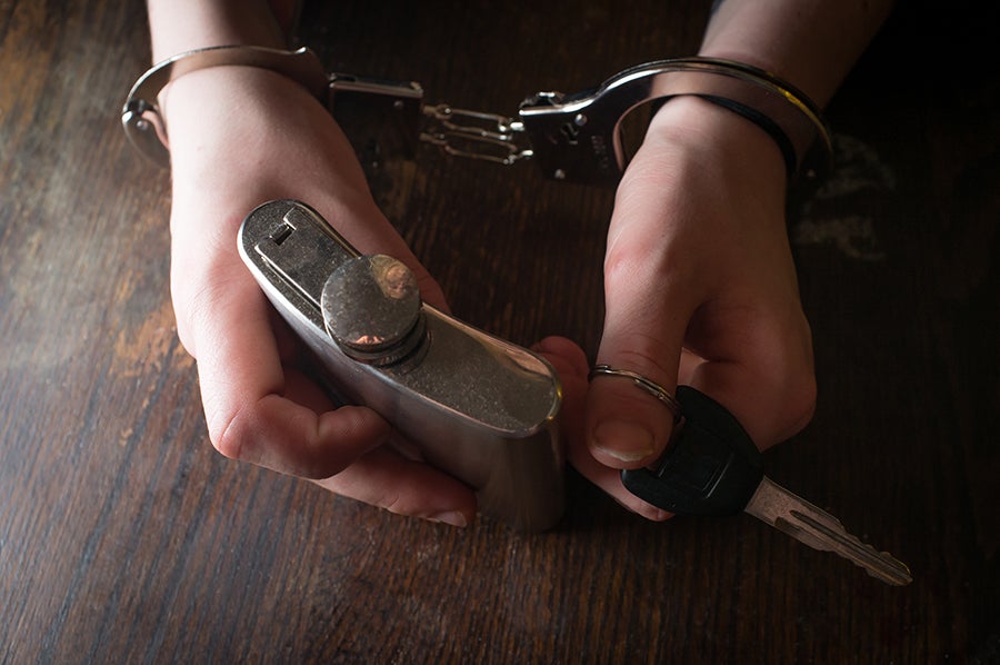 Hands in handcuffs hold a flask and car keys on a dark wooden table, symbolizing drunk driving consequences.