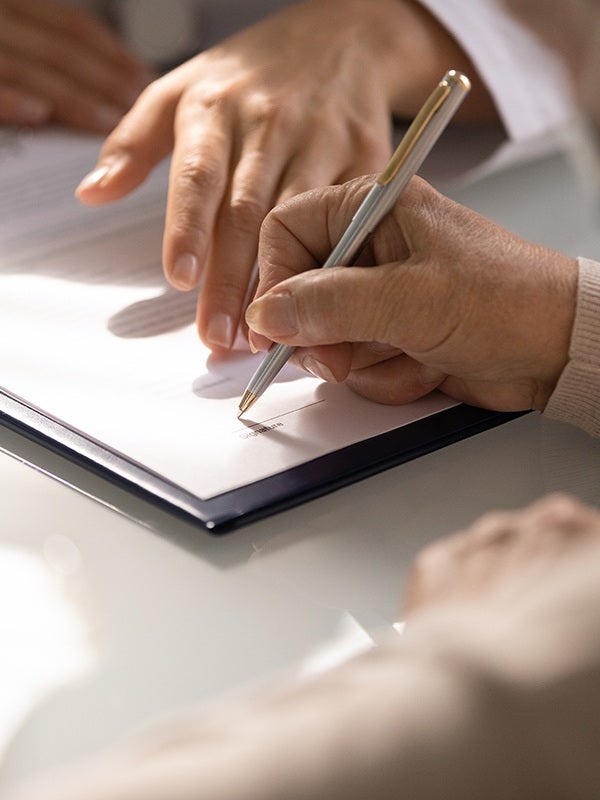 RA person's hand signing a document labeled signature with a pen another hand resting nearby.