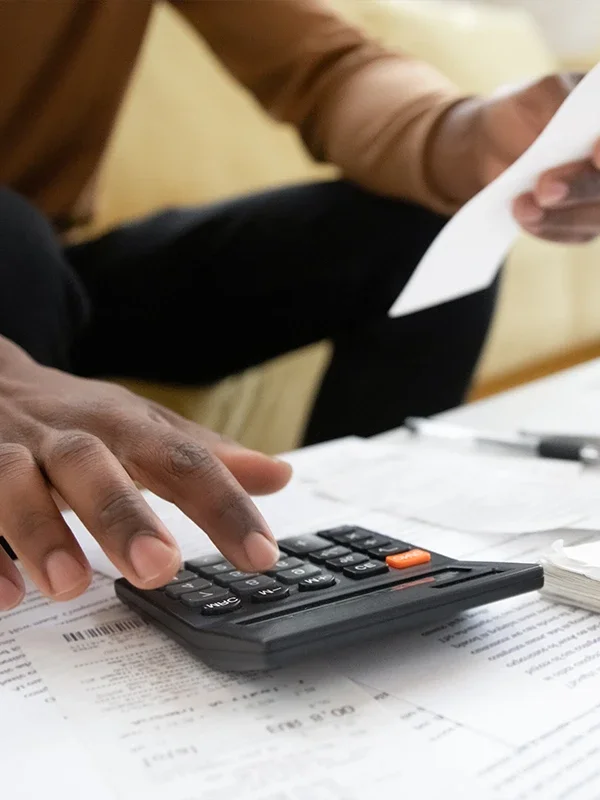 A person uses a calculator, surrounded by papers and a pen, with another document in their left hand.