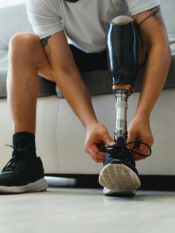 A person with a prosthetic leg ties their shoe, sitting on a sofa in a close-up shot.
