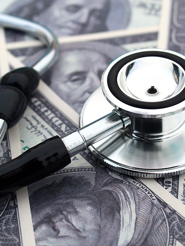 A stethoscope lies across several hundred-dollar bills, symbolizing healthcare costs.
