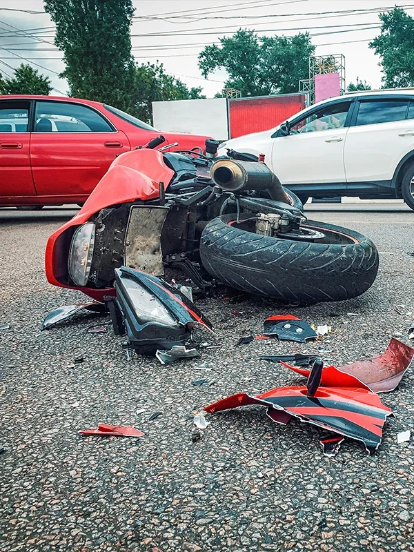 A totaled red motorcycle lies on its side on a paved road with broken pieces scattered around it.