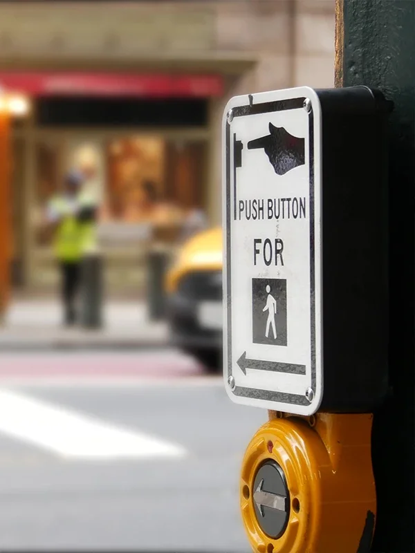 A black and white Push Button for Pedestrian sign with a yellow push button attached to a lamppost.