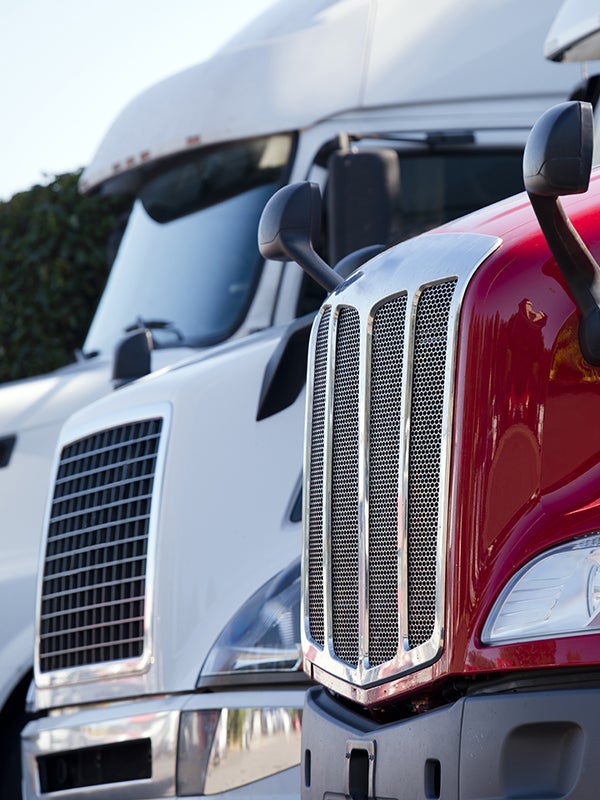 Front grilles and headlights of a red semi-truck next to a white semi-truck.